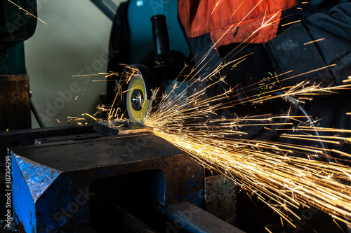 Fotomural The worker cuts the workpiece, sparks fly in different directions