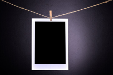 Close-up of blank polaroid photographs hanging on a clothesline in black room.