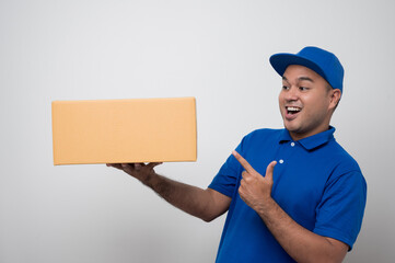 Wall Mural - Young smiling asian delivery man in blue uniform holding box parcel cardboard on isolated white background.