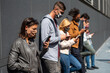 © MandriaPix - young Caucasian woman who reads and inquires about the corona virus infection in the foreground, group of multi-ethnic friends addicted to the use of cell phone, all wear protective masks, new normal