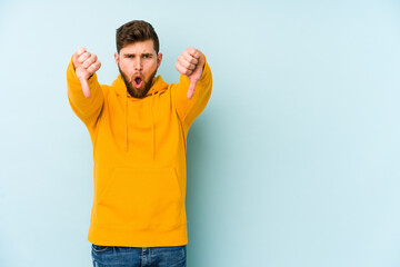 Wall Mural - Young caucasian man isolated on blue background showing thumb down and expressing dislike.