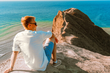 Canvas Print - A man in a white shirt sits on the slope of Cape chameleon with an amazing panoramic view of the hills and the sea from above