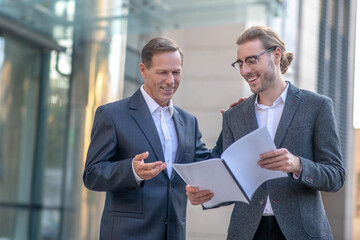 Two involved male colleagues studying documents, having discussion outside