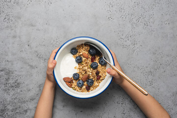 Child's hands holding a bowl of morning breakfast. Homemade granola with yogurt and blueberries. Healthy quick snack