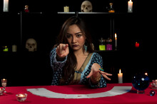 Portrait Of Asian Beautiful Gypsy Fortune Teller Woman In Dark Room With White Tarot Card And Pointing Finger To Camera. Focused On Face.