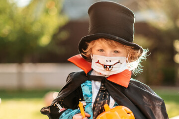 Happy Halloween. A child in a medical mask in a dracula costume sits on a pumpkin in his yard.