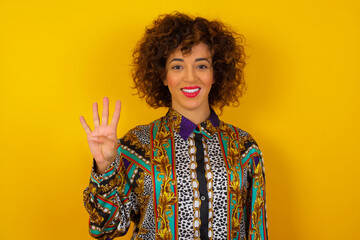 Wall Mural - Young   woman standing against gray wall showing and pointing up with fingers number four while smiling confident and happy.