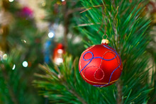 Red Ball On Green Spruce Branches On A Blurred Background. Christmas And New Year Decorations. A Bauble On The Tree. Shallow Depth Of Field