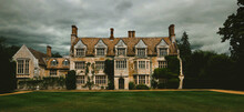 Panoramic, Spooky Old English Manor House With Lawn Trees. Dramatic Cloudy And Overcast Sky 