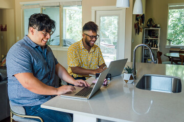 Wall Mural - gay couple working from home on laptop computers sitting at kitchen counter