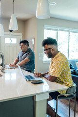 Wall Mural - gay couple working from home on laptop computers sitting at kitchen counter