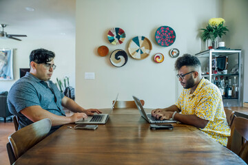 Wall Mural - gay couple working from home together on laptop computers sitting at dining room table