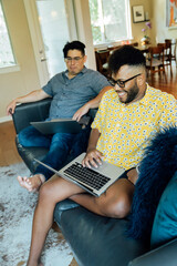 Wall Mural - happy gay couple working from home with laptop computers, sitting on couch