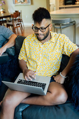 Wall Mural - happy gay couple working from home with laptop computers, sitting on couch