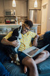Man working from home with laptop sitting on couch and petting happy Australian Shepherd pet dog
