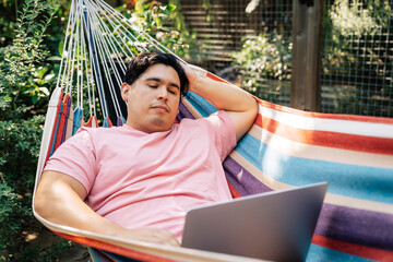 Wall Mural - man relaxing in hammock working on laptop computer