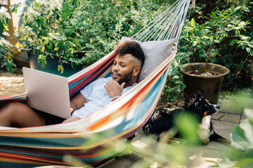 Wall Mural - man relaxing in hammock working on laptop computer