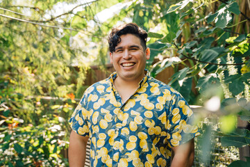 Wall Mural - Portrait of happy, smiling latinx man in bright patterned shirt standing outside in garden