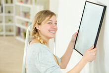Woman Hanging Blank Picture On Wall