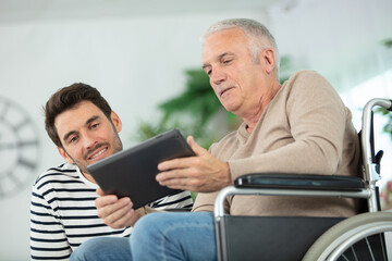 man in wheelchair showing tablet to male companion