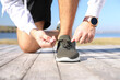 © New Africa - Sporty man tying shoelaces near river on sunny morning, closeup
