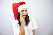 Young Beautiful Woman Wearing A Christmas Hat Over White Background Pointing To The Eye Watching You Gesture, Suspicious Expression