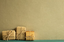 Gift Boxes Wrapped In Kraft Paper On Wooden Table With Khaki Green Background. Anniversary, Birthday, Christmas Concept