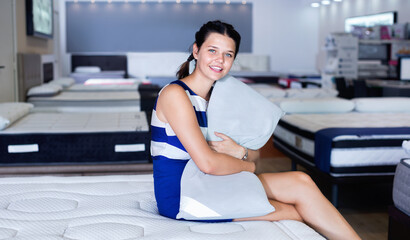 Wall Mural - Young happy cheerful positive woman is sitting on bed with new pillow in the store.