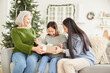 © AnnaStills - Little girl getting Christmas present from her mother and sister sitting on sofa at home