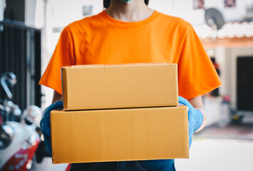 Delivery woman wearing an orange T-shirt, holding parcel boxes before delivering to customer. Conceptual shot of parcel delivery while working.