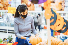 Young Woman Wearing A Protective Mask And Gloves Choosing Pumpkins For Halloween In A Supermarket. Reality 2020