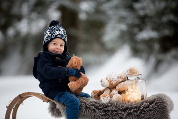 Poster - Cute boy playing with teddy bear in the snow, winter time. Little toddler playing with toys on snowy day