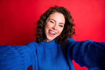 Closeup photo of cute pretty lady curly hairdo take selfie having fun tongue-out blink eye lick teeth carefree wear blue knitted sweater pullover jumper isolated red color background