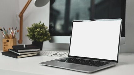 Comfortable workplace. A computer laptop with white blank screen, notebook and plant on modern white working desk.