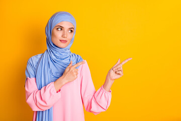 Portrait of attractive content smart muslimah wearing hijab demonstrating aside advert copy space isolated over bright yellow color background
