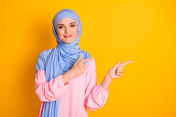 Portrait of attractive content cheery muslimah wearing hijab demonstrating new novelty copy space isolated over bright yellow color background