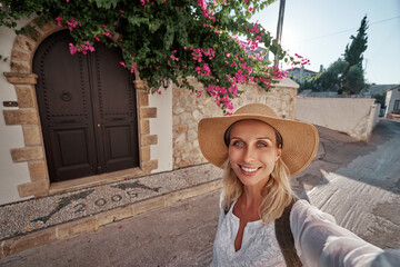 Travel by Greece, Young woman in hat with rucksack taking selfie near traditional greek house.