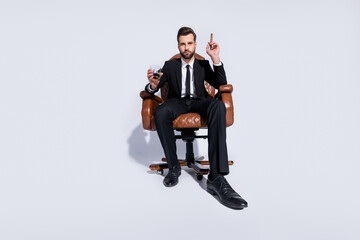 Sticker - Full size low angle view photo of handsome business guy sit office chair hold whiskey glass cuban cigar luxury chief wear black blazer pants tie shirt shoes suit isolated grey background