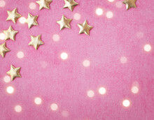 Christmas Ornaments, Shiny Golden Stars And Christmas Lights On Pink Paper Background