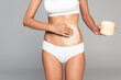 © LIGHTFIELD STUDIOS - Cropped view of woman in white underwear holding jar and applying cream on belly isolated on grey