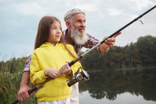 Happy Senior Man Enjoying Teaching His Granddaughter Fishing At The Lake, Copy Space