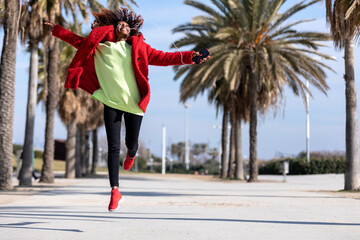 Young black woman with afro hairstyle jumping in urban background.