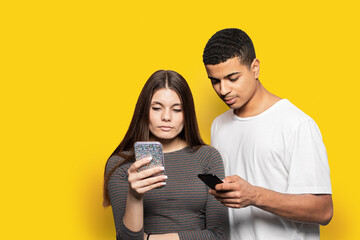 Photo of two funny guy lady people couple hold telephones arms interested reading social network article wear casual t-shirts isolated yellow color background