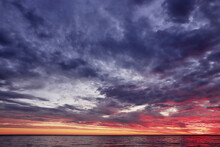Beautiful Sunset On The Sea, Dramatic Sky With Dark Blue Clouds. Smooth Sea Horizon In Red And Orange Lighting