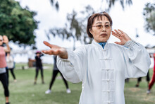 Mature Chinese Woman Do Tai Chi With Blirred Group Of People Outdoor In The Park