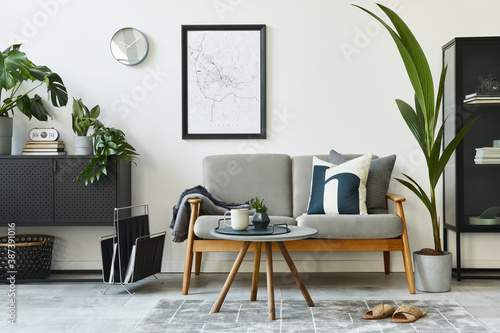 Modern retro concept of home interior with design grey sofa, coffee table, plants, furniture, mock up poster map, decoration and personal accessoreis. Stylish home decor of living room.