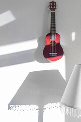 Red Ukulele on the white wall in the morning sunlight