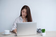 © PaeGAG - Young Asian women wear headphones using their laptop inside the office, working for online lessons or listening to webinars.