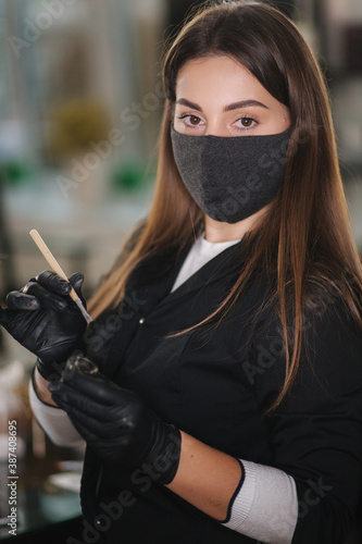 Portrait of professional female brow master in black robe with black gloves and black protective mask use brush and henna for eyebrows