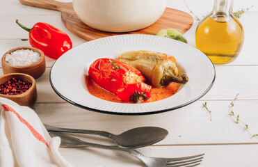 Pepper stuffed with minced chicken meat and rice in a white plate on a white wooden table.